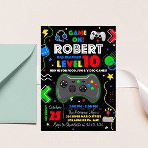 K&ouml;nnte beinhalten: Eine schwarze und neongr&uuml;ne Videospiel-Geburtstagseinladung zum 10. Geburtstag von Robert. Die Einladung zeigt einen gro&szlig;en schwarzen und gr&uuml;nen Videospiel-Controller, den Text "GAME ON!" und "ROBERT HAS REACHED LEVEL 10" sowie das Datum und die Uhrzeit der Party.