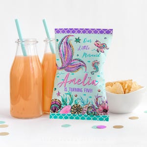 Puede incluir: Una bolsa de regalo para fiestas de temática de sirena azul verdoso y morado con una cola de sirena rosa brillante, un caballito de mar y una tortuga. La bolsa dice "Nuestra pequeña sirena Amelia cumple cinco años!"