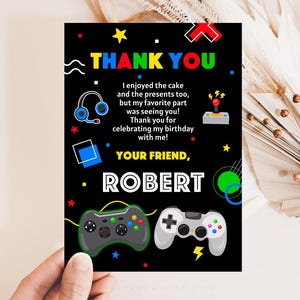 K&ouml;nnte beinhalten: Eine schwarze Dankeskarte mit buntem Text und Grafiken. Die Karte zeigt einen Videospiel-Controller, Kopfh&ouml;rer und den Text "THANK YOU" und "YOUR FRIEND, ROBERT".
