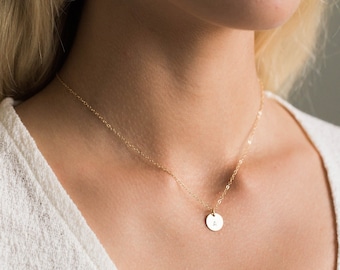 May include: A gold chain necklace with a small round pendant featuring a single letter.