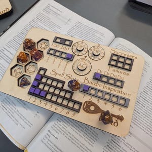 May include: A wooden tabletop gaming organizer with laser-cut designs. It features slots for dice, spell tracking, and other game components. The organizer is placed on top of an open book, with dice and other game accessories.