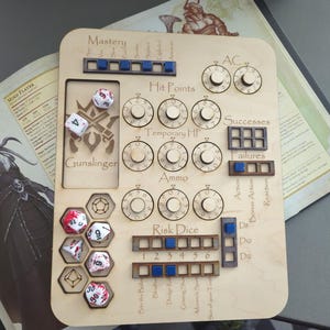 May include: A wooden tabletop gaming board with various slots for dice and dials. The board includes sections for "Hit Points," "Ammo," and "Risk Dice." Several dice are placed on the board, along with the text "Gunslinger."