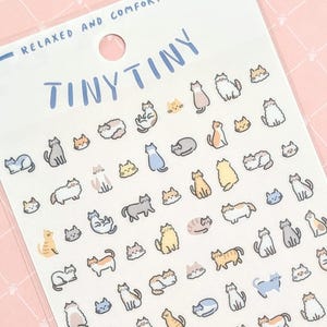 May include: A sheet of stickers featuring tiny illustrations of cats in various poses and colors. The stickers are on a white background and have the text "Tiny Tiny" and "We Are Neko" printed on them.