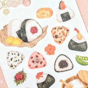 May include: A sheet of stickers featuring various Japanese onigiri (rice balls) with different fillings, including salmon, seaweed, and pickled plum. The stickers are part of the Iroha Seal collection.