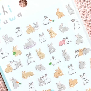 May include: A sheet of stickers featuring numerous small, illustrated rabbits in various poses and colours, including brown, white, and grey. The top of the sheet displays the text Puchi fuwa and -Usagi- in a light blue font on a white background.