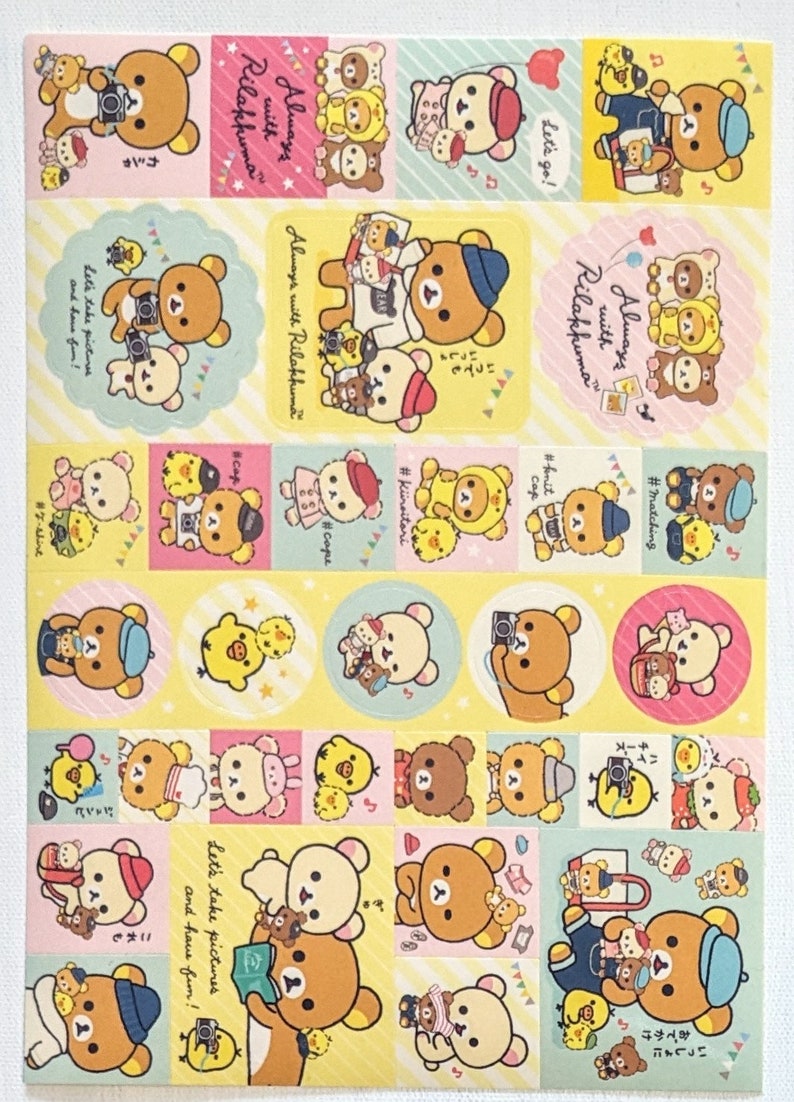 May include: A sheet of colourful stickers featuring the Rilakkuma bear character in various poses. The stickers have a yellow, pink, and blue colour scheme, with text that says "Always with Rilakkuma" and "Let's take pictures and have fun!"