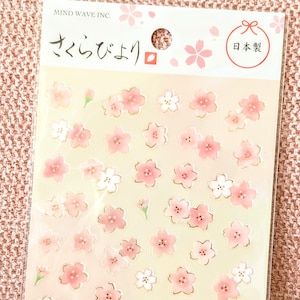 Peut inclure: Une feuille d'autocollants avec des motifs de fleurs de cerisier roses et blanches. Les autocollants ont un contour doré et sont de différentes tailles. L'emballage comprend du texte japonais et les mots "Mind Wave Inc."