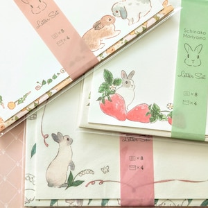 May include: Letter sets with bunny and floral illustrations. Each set contains stationery with bunny and strawberry graphics, and the text "Letter Set". The sets are packaged with pink and green bands.