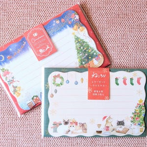 May include: Two Christmas-themed stationery sets. One features a red border with a winter scene and a Christmas tree. The other has a green border with a cat illustration and Christmas decorations. Each set includes lined paper.