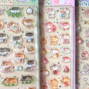 Op de afbeelding: Drie verticale vellen met opgeblazen, doorschijnende stickers met diverse dierfiguren. Het linker vel toont bruine en zwarte honden, het middelste vel katten met fruitmotieven en het rechter vel bevat konijnen en sterren.