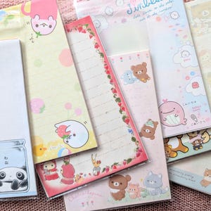 Peut inclure: Plusieurs blocs-notes illustrés avec des personnages de dessins animés et des motifs variés. Les blocs-notes présentent des pandas, des ours, des fraises et d'autres éléments mignons. Certains blocs-notes ont des pages lignées, d'autres sont vierges.