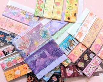 May include: A collection of colorful washi tapes with various designs, including floral patterns, planets, animals, and musical notes. The tapes are arranged in a pile on a pink surface.
