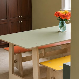 May include: A light green rectangular table with two benches, one orange and one yellow. The table and benches are made of light wood. A vase of orange and yellow roses sits on the table. The table is approximately 72 inches long.