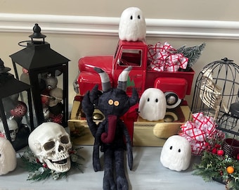 May include: A collection of Halloween decor featuring a red metal truck, a black plush horned creature with button eyes, a human skull, four white fuzzy ghost figures, two black lanterns filled with ornaments, and a black wire birdcage.