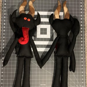 Two black fabric Krampus characters with long limbs and horns.  One is facing forward the other showing the backside.