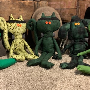 May include: Five plush toys with green, yellow, and black fabric. The toys have button eyes and are sitting on a carpet.