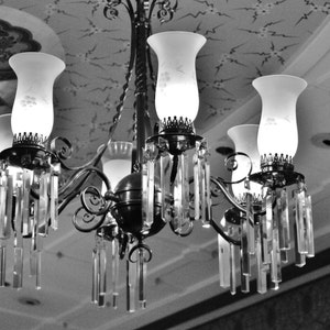 May include: A black and silver chandelier with five frosted glass light bulbs and crystal accents. The chandelier is hanging from a ceiling with a decorative pattern.