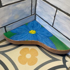 May include: A wooden corner shelf painted with a blue flower with a yellow center and green leaves.