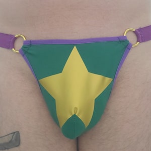 Könnte beinhalten: Grüne Unterwäsche mit einem violetten Saum und einem großen goldenen Stern in der Mitte.