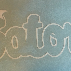 May include: White vinyl decal with the word "Gators" in a stylized font with a white bow on top of the first letter.