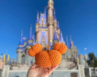 May include: A crocheted pumpkin shaped like Mickey Mouse's head with orange pumpkins for ears in front of Cinderella's Castle at Walt Disney World.
