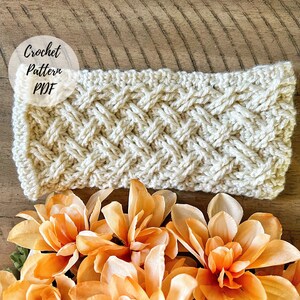 以下が含まれることがあります： クリーム色のクロシェヘッドバンドのパターンで、白い円の中に「Crochet Pattern PDF」というテキストが書かれています。ヘッドバンドは、オレンジの花が咲いた木製の表面の上に置かれています。