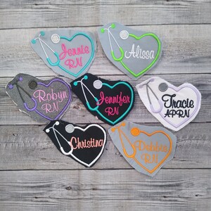 May include: Six heart-shaped embroidered patches with a stethoscope design and names, including 'Jennie RN', 'Robyn RN', 'Jennifer RN', 'Alissa', 'Tracie APRN', and 'Debbie RN'.