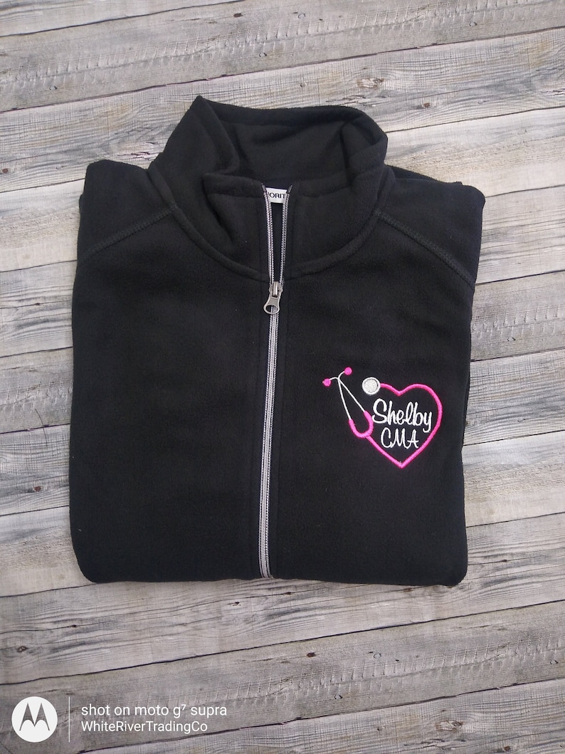 May include: Black fleece zip-up jacket with a pink embroidered stethoscope and heart with the text "Shelby CMA".