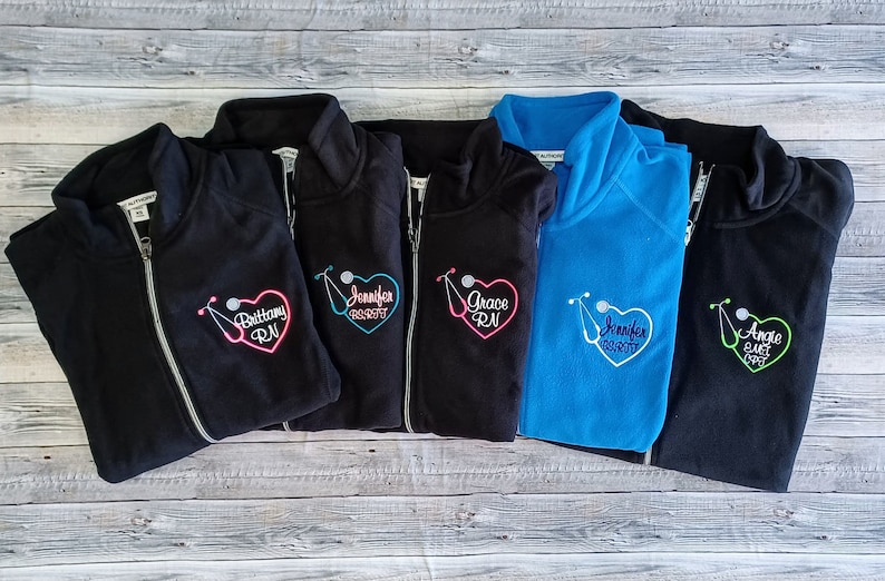 May include: Five black fleece jackets with a zipper closure and a stethoscope and heart design embroidered on the left chest. The embroidery includes the names "Brittany RN", "Jennifer RN", "Grace RN", "Jennifer RN", and "Angie EMT RN".