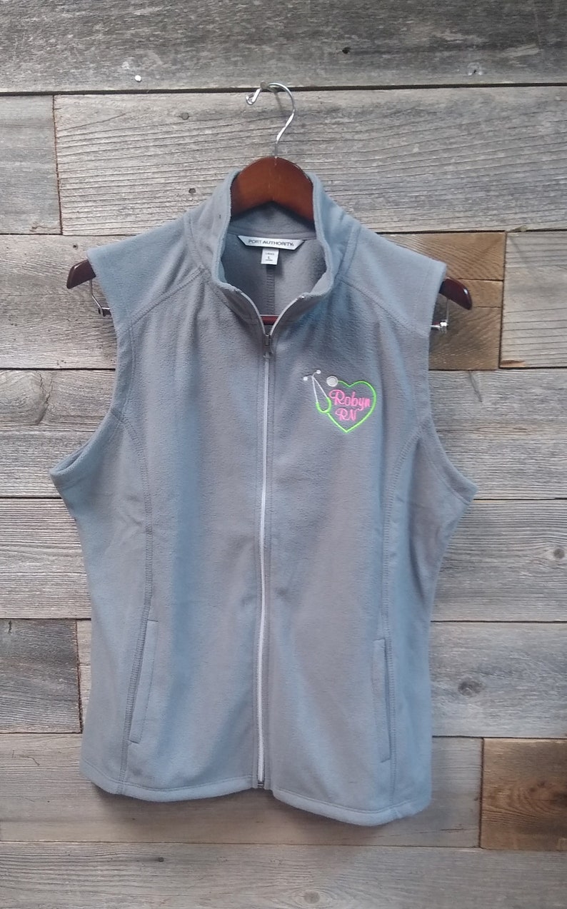 May include: Gray fleece vest with a zipper closure and a pink heart with a stethoscope and golf ball graphic that says "Robyn RN".