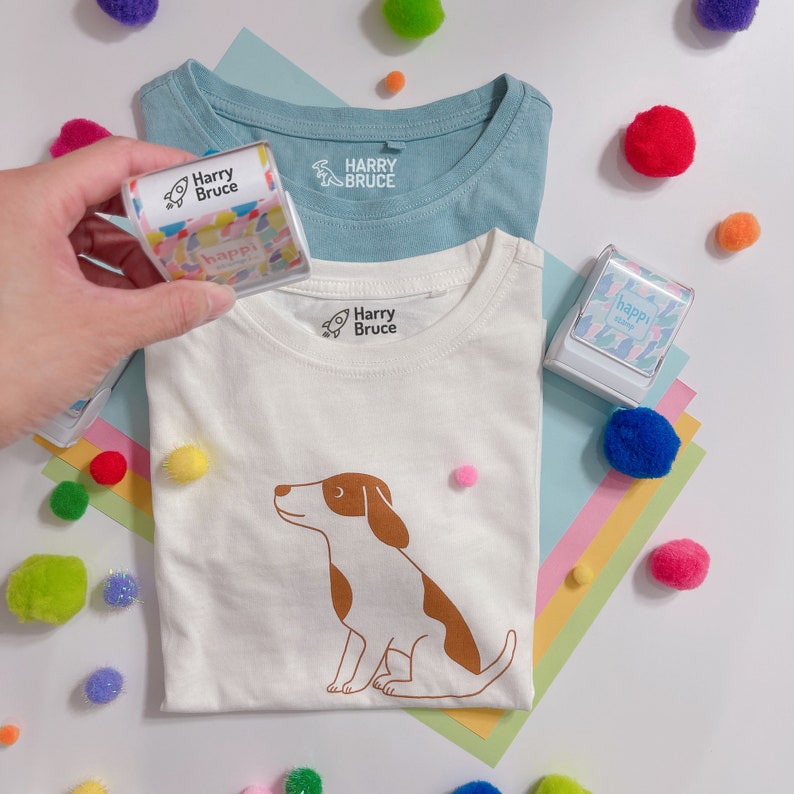 A woman hand holding  a fabric name stamp with black ink from Happi Stamp Co Australia tried to label on a white tee shirt.