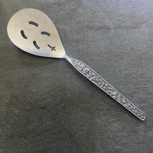 Peut inclure: Une cuillère ajourée en argent avec un motif floral sur le manche. La cuillère a une tête ovale avec quatre fentes ovales et une en forme de croix. La poignée est ornée de fleurs et d'étoiles.