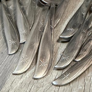 Peut inclure: Gros plan sur des couverts anciens avec un motif en forme d'éclat d'étoile. Les cuillères et les fourchettes sont en métal brillant de couleur argentée. Les ustensiles sont disposés sur une surface en bois, mettant en valeur leurs détails complexes et leur style classique.