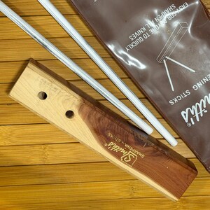 May include: A wooden knife sharpening system with two white and gray sharpening rods. The wooden base has a light wood color with a darker wood accent. The packaging reads "Easy for anyone to quickly sharpen all knives."