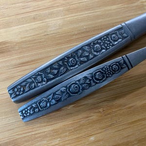 Peut inclure: Deux pièces de couverts argentées avec un motif floral orné. Le motif présente un motif répétitif de roses et de feuilles.