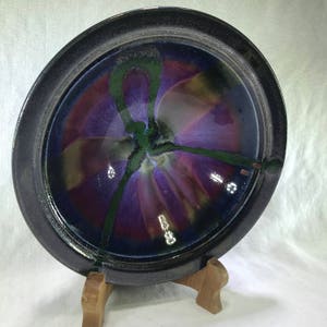 May include: A black ceramic bowl with a purple and green floral design. The bowl is on a wooden stand.