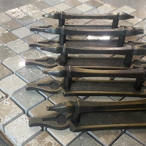 May include: Five antique brass cabinet door pulls with ornate designs. The pulls are arranged in a stack, with the largest pull at the bottom and the smallest pull at the top.