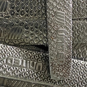 May include: Close-up of a stack of silver bars with the word "UNITED" embossed on each bar. The bars have a textured surface with a repeating pattern of small circles.