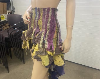 May include: A multi-colored, high-low skirt with a ruffled hem. The skirt is made of a variety of fabrics, including purple, yellow, and brown. The skirt is asymmetrical, with one side being longer than the other.