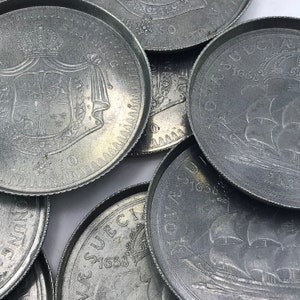 Könnte beinhalten: Nahaufnahme einer Sammlung von Silbermünzen mit verschiedenen Designs, darunter ein Wappen und ein Schiff. Die Münzen haben erhöhte Ränder und komplizierte Details.