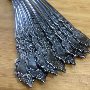 Puede incluir: Un juego de cucharaditas plateadas con un diseño floral. Las cucharas tienen un mango decorativo con un patrón de rosas.