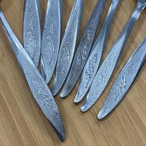 May include: A set of eight silver-toned forks with a floral design. The forks are arranged in a fan shape on a wooden surface.