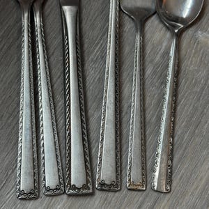 以下が含まれることがあります： フォークとスプーンを含む、ヴィンテージの銀食器のセットのクローズアップ。銀食器は銀色で、柄に精巧で詳細な模様が施されています。木製の表面に配置された食器です。