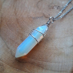 Puede incluir: Un collar de cadena de plata con un colgante de cristal de ópalo blanco envuelto en alambre de plata.