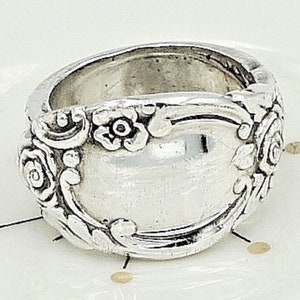May include: A silver ring made from a repurposed spoon with a floral design. The ring is wide and has a smooth, rounded surface.