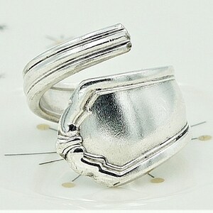 May include: A silver spoon ring, crafted from a vintage spoon, with a unique curved design. The ring is made from a single piece of metal, with the spoon's bowl forming the top of the ring.