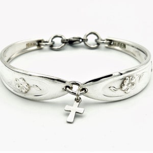 May include: A silver bracelet made from a spoon with a floral design and a small cross charm.
