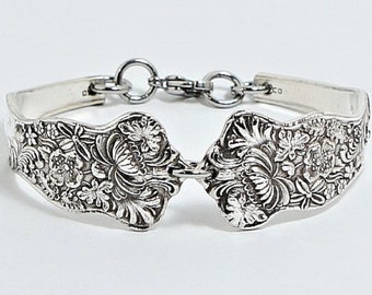 May include: A silver bracelet made from two ornate spoons connected by a chain. The spoons are decorated with a floral pattern.