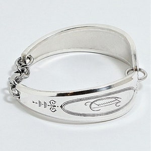 May include: A silver bracelet made from a repurposed spoon. The bracelet has a chain link closure and an engraved design on the spoon part.