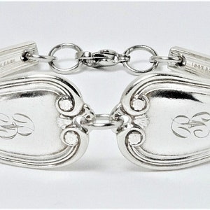 May include: A silver bracelet made from a vintage spoon with an engraved monogram. The bracelet is connected with a silver chain and clasp.